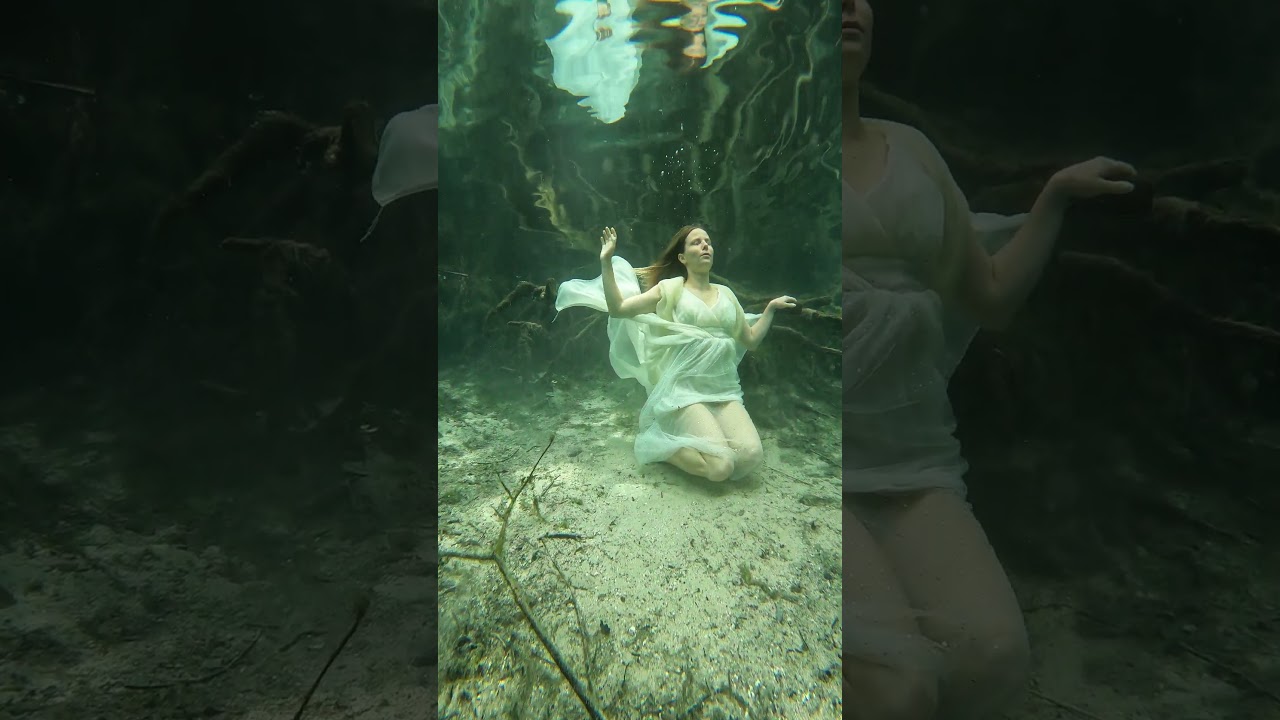 Elegantly posing beneath the surface of the water in a white dress.