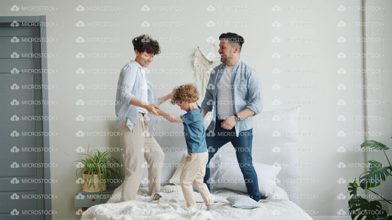 Mother father and son jumping dancing on bed in bedroom at home together