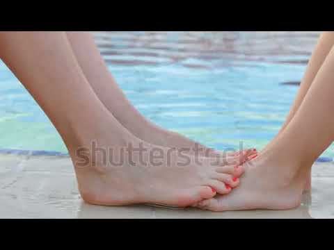 Stock close - up of the mother and daughter playing their bare feet of water near the pool