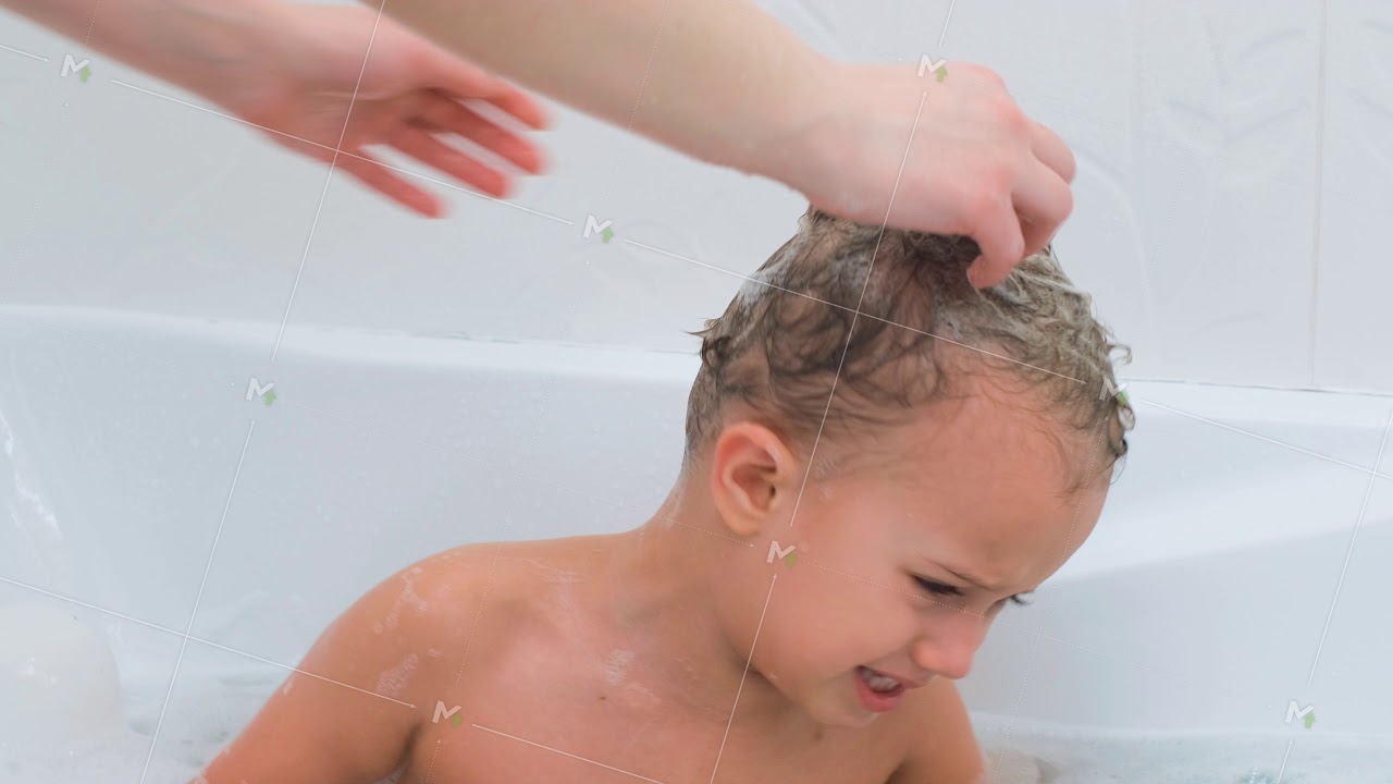 The little boy starts to get angry while bathing. Mom's hands try to wash the boy's hair with